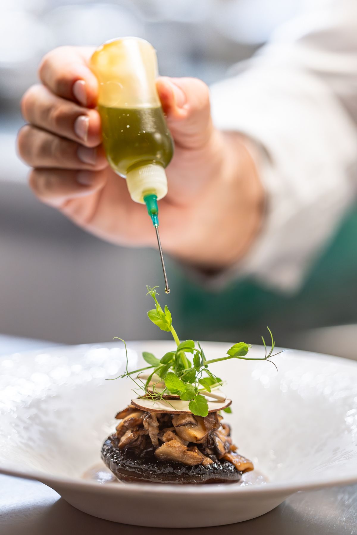 Main de chef déposant une sauce verte à la pipette sur une assiette